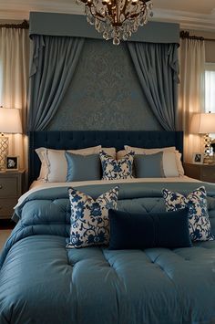 a bed with blue comforter and pillows in a bedroom next to two lamps on either side of the bed