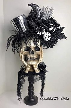 a skull wearing a black hat with feathers and flowers on it's head, sitting in front of a white wall