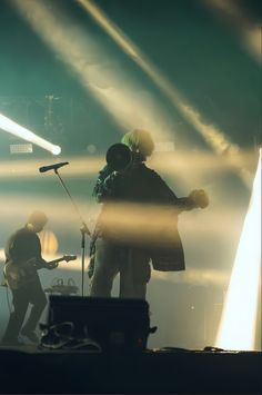 two people standing on stage with microphones in front of them and one person playing the guitar