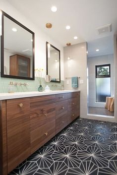 a bathroom with black and white tile flooring and wooden cabinetry, along with two large mirrors on the wall