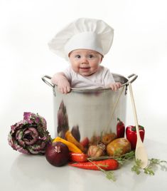 a baby in a chef's hat is sitting in a pot filled with vegetables