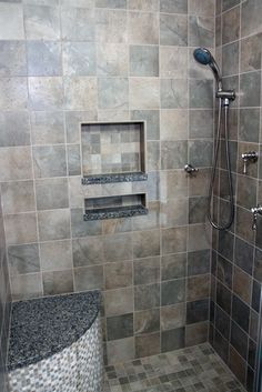 a walk in shower sitting next to a tiled bathroom wall with gray tiles on the walls