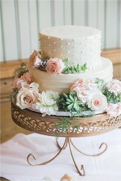 a three tiered wedding cake with pink and white flowers on the top, sitting on a gold stand