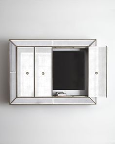 a mirror mounted on the wall with a television in it's center section and doors open