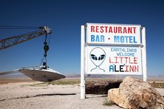 a sign that says restaurant bar motel and an alien boat is on the ground next to it