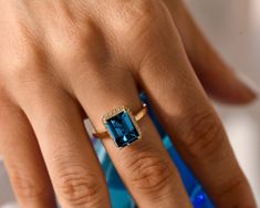 Discover our gorgeous London Blue Topaz ring! It's a deep blue, natural gemstone with stunning color and clarity. The emerald cut weighs about 3.5 Ct. The ring features a unique semi-hidden halo, with options for Diamond or Moissanite. Perfect as a December birthstone gift, or a dazzling proposal or engagement ring. It's also a great anniversary present. Explore our fine jewelry collection today. Enjoy its beauty, charm, and elegance - it's designed just for you!  ★ ★  CUSTOM/DUTY-FREE SHIPPING One Year Anniversary Gift, Vintage Promise Ring, Birthstone Engagement Rings, Hidden Halo Ring, Promise Rings Vintage, December Birthstone Ring, One Year Anniversary Gifts, Blue Topaz Engagement Ring, London Blue Topaz Ring