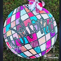 a painted ball with the word welcome on it in front of some flowers and grass