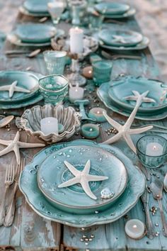 the table is set with starfish plates and silverware, candles and seashells