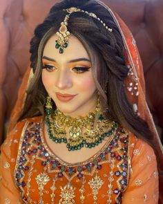 a woman in an orange and gold bridal outfit with jewelry on her head, sitting down