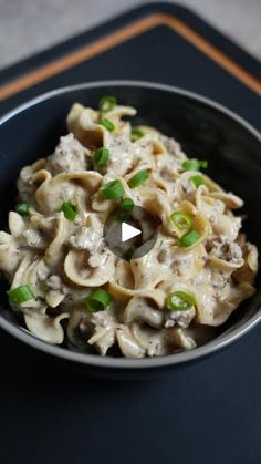 a bowl filled with pasta and green onions on top of a table next to a black mat