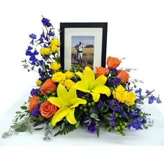 a vase filled with yellow and blue flowers next to a framed photo on a table