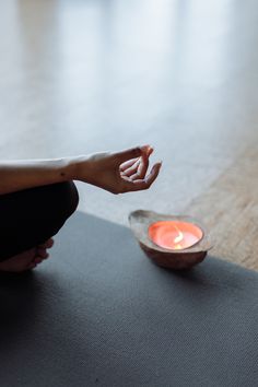 a person sitting on a yoga mat in front of a bowl with a lit candle