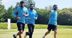 three men in blue shirts and black shorts running on a field