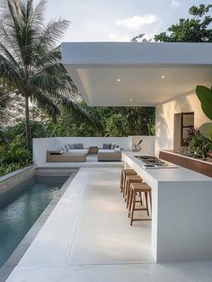 an outdoor kitchen next to a swimming pool with bar stools on the counter top