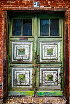 an old wooden door with green paint on the outside and brick wall behind it, in front of a red brick building