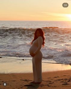 a pregnant woman standing on the beach at sunset