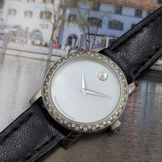 This ladies Movado wristwatch is a chic addition to any collection. The diamond and silver bezel adds a touch of luxury to the pearl white dial and black leather strap. With a quartz movement and sapphire crystal feature, this wristwatch is both reliable and stylish. The reference number of 84E418361S indicates its authenticity and origin from Switzerland. new battery and leather strap installed Elegant White Diamond Watch For Evenings, Elegant White Diamond Watch For Evening, Luxury White Diamond Watch For Evening, Luxury White Watches With Leather Strap, Elegant Leather Round Watch, White Analog Diamond Watch, White Round Analog Diamond Watch, Elegant White Watches With Metal Dial, Timeless White Watches For Evening