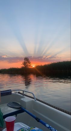 the sun is setting on the water as a person sits in a boat with a drink