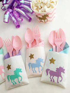 pink and purple plastic utensils with unicorns on them next to a bag of popcorn