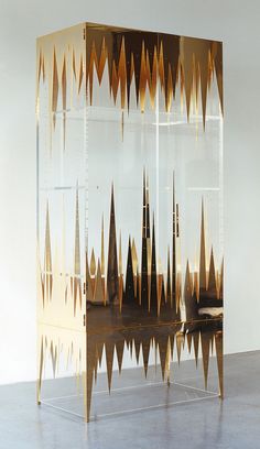 an artistic display case with gold and brown designs on the front, in a white room