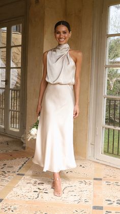 a woman in a white dress standing next to an open door and smiling at the camera