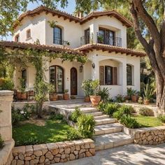 a large white house with lots of windows and plants in the front yard, along with steps leading up to it