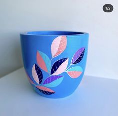 a blue bowl with leaves painted on the outside and inside, sitting on a white surface