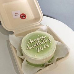 a green birthday cake in a white box on a table with the lid open to show it's frosting