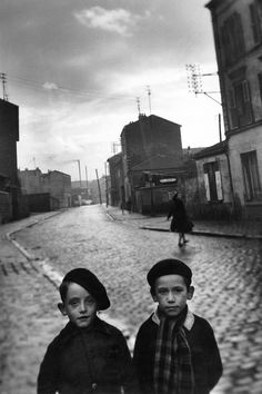 two young boys are standing in the middle of an alleyway with buildings on either side