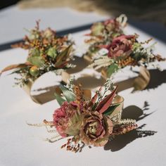 three boutonnieres with flowers on them sitting on a white cloth tablecloth