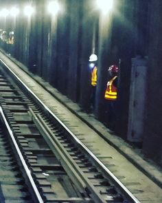 two men in yellow vests are standing on the train tracks next to each other