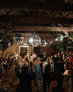 a large group of people dancing at a party with disco balls hanging from the ceiling