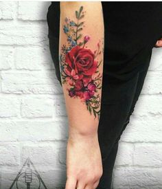 a woman's arm with flowers on it and an arrow in the middle, next to a brick wall