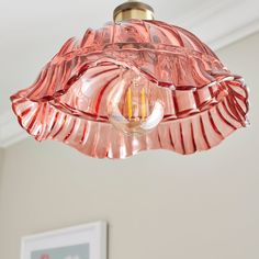 a pink glass light fixture hanging from a ceiling in a room with a framed photograph on the wall