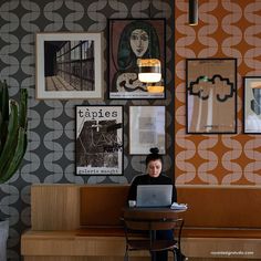 a woman sitting at a desk with a laptop in front of her and many pictures on the wall behind her