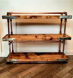 three tiered wooden shelf with metal pipes on the top and bottom, against a white wall