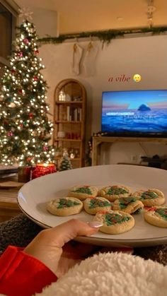 a person is holding a plate with cookies on it in front of a christmas tree