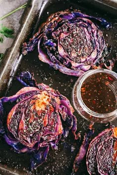 grilled artichokes on a baking sheet with dipping sauce in a glass jar