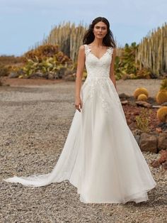 a woman in a white wedding dress standing on gravel with cacti behind her