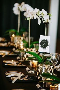 the table is set with black and gold plates, silverware, and orchid centerpieces