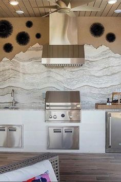 an outdoor kitchen with stainless steel appliances and large wall art behind the stove top oven