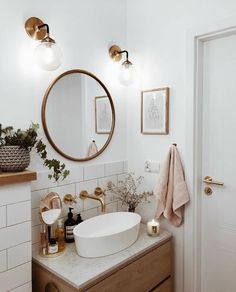 a bathroom with a round mirror above the sink and gold faucet lights on the wall