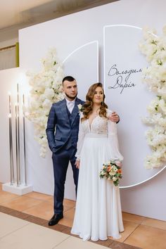 a man and woman standing next to each other in front of a wall with flowers