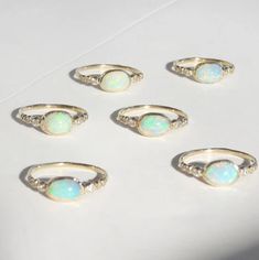 six opal rings sitting on top of a white table next to eachother