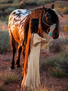 a woman is petting a brown and white horse in the desert with long hair