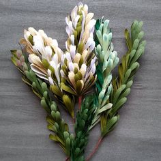 three different types of fake flowers on a gray tablecloth with green stems and leaves