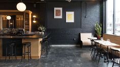 the interior of a restaurant with black walls and wooden bar stools, wood tables, and hanging lights