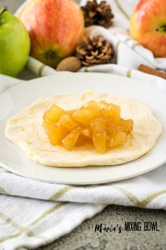 an apple pie on a white plate next to some apples and pineconi in the background