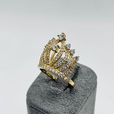 a gold crown ring sitting on top of a gray velvet box with white and yellow diamonds