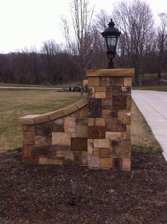 a lamp post sitting on top of a stone wall next to a sidewalk and grass field